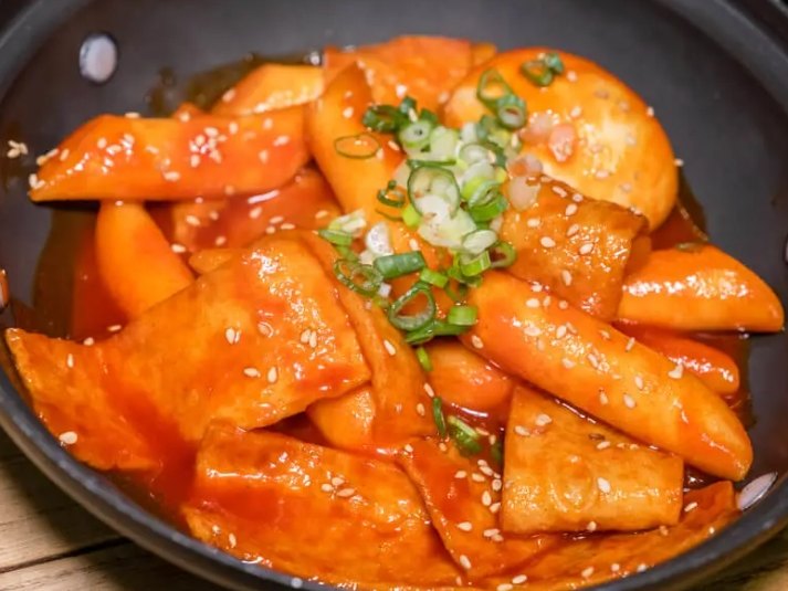料韓男的辣炒年糕，鐵鍋盛裝，撒上芝麻和蔥花
